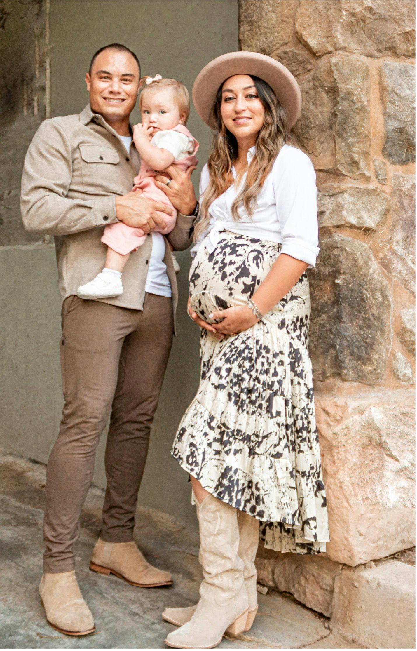 A pregnant Maresa King standing next to her husband who is holding their daughter