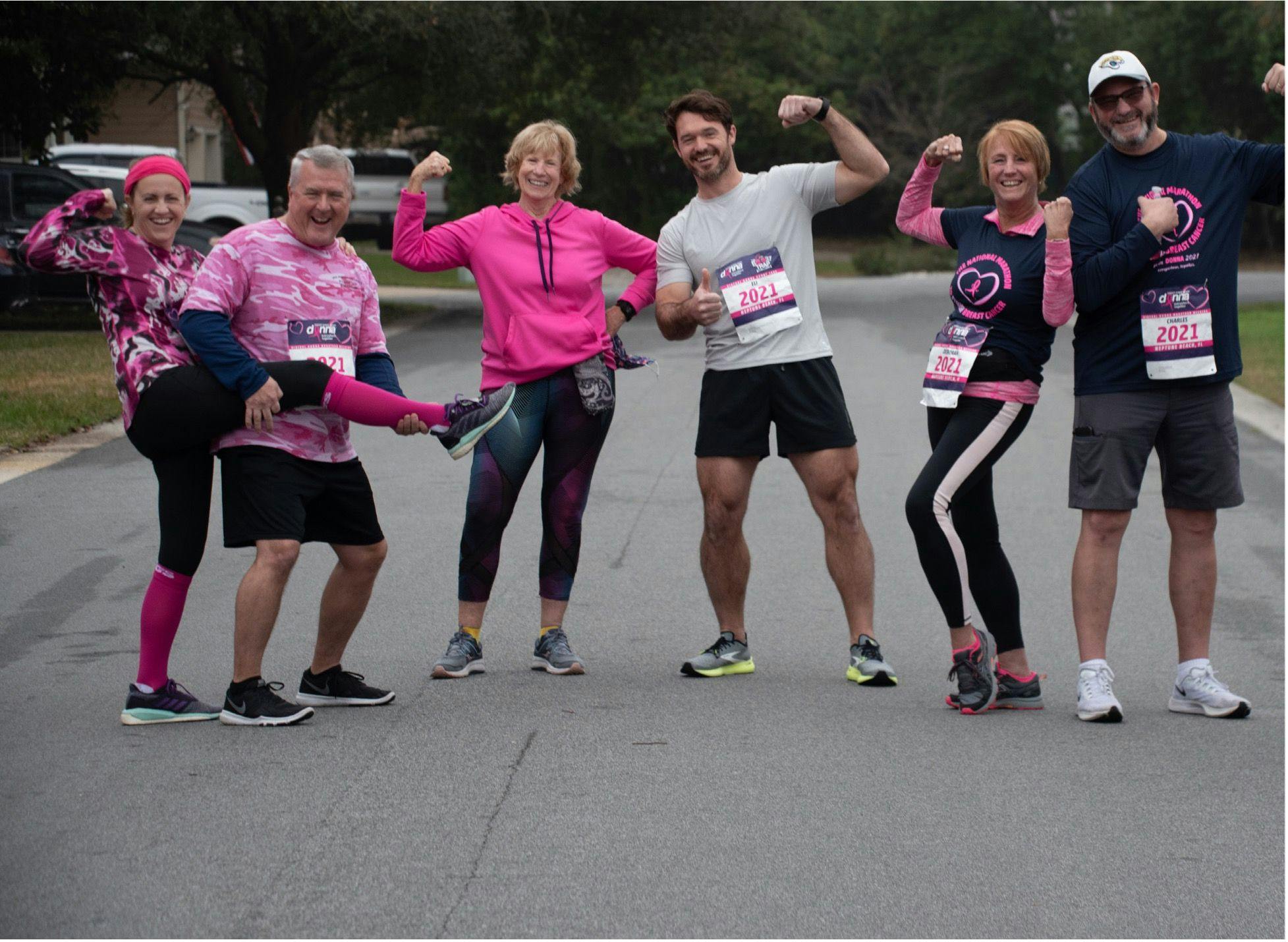six adults dressed in pink smiling and making a muscle in the middle of the street